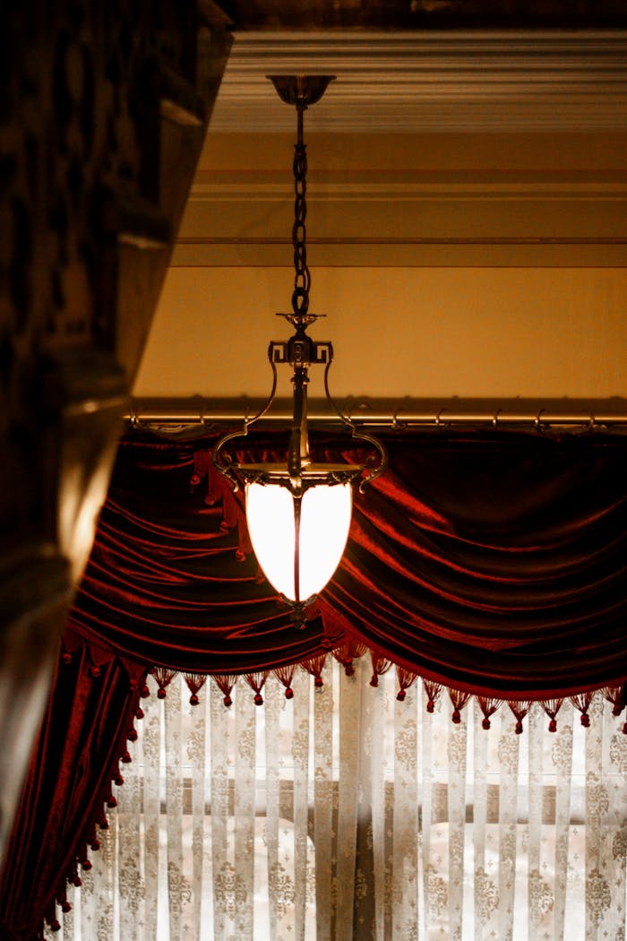 A beautifully lit chandelier in a sophisticated vintage room with red velvet curtains.